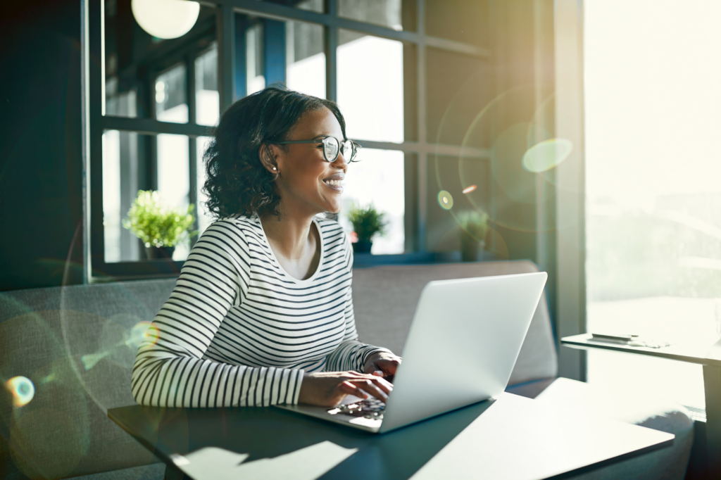 Atmospheric photo of a woman sitting at a long booth at a restaurant, smiling, relief, typing on her laptop, concept photo of a business owner that has made a financial decision to address financial distress