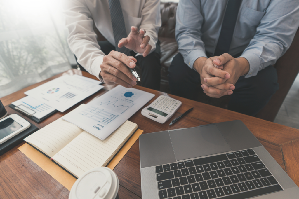 Cropped photo of business partners sitting together in front of a desk, laptop, and documents, discussing loans for tax debt, business loans, and solutions for ATO tax debt