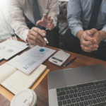 Cropped photo of business partners sitting together in front of a desk, laptop, and documents, discussing loans for tax debt, business loans, and solutions for ATO tax debt