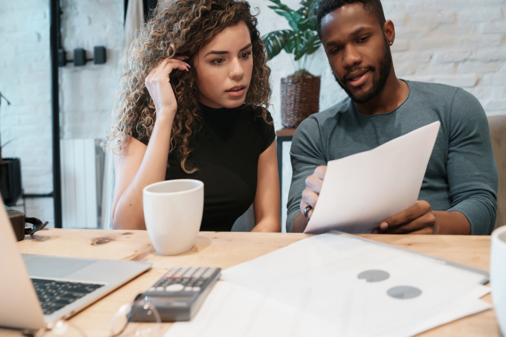 Business owner couple worriedly examines tax document, tax debt, considering tax debt loans, man and woman sitting, laptop, cup, and documents visible on table