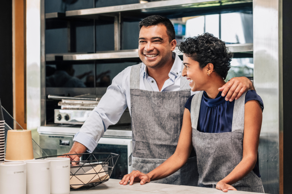 Business owner couple smiling inside their place of business, cafe, owners in aprons, happy couple, concept photo of business owners who found a suitable tax debt loan solution