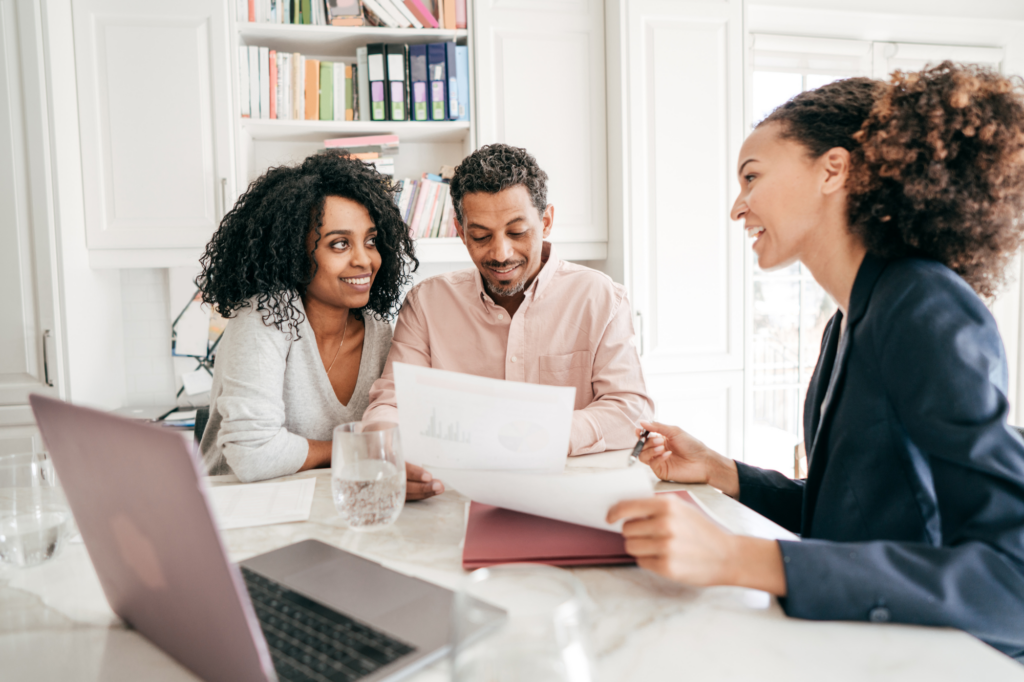 Couple smiles, the man looks at a piece of paper while the woman smiles at another woman sitting across them, concept photo of business owners getting their business loan approved