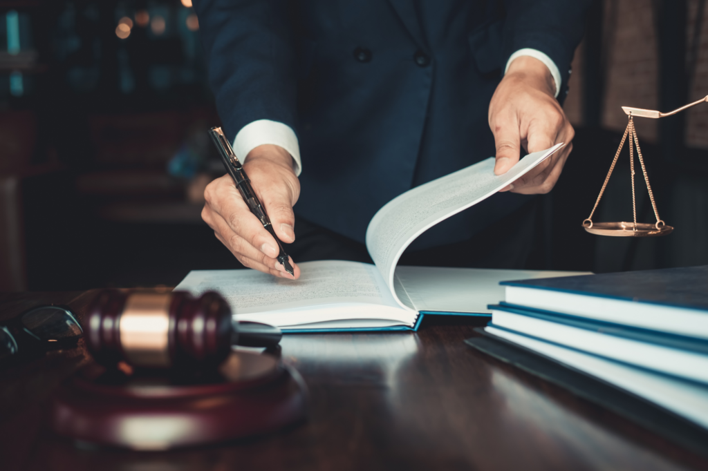 Concept photo of lawmaker signing legislation into effect, cropped photo of man in suit signing documents on table, gavel and law scales visible