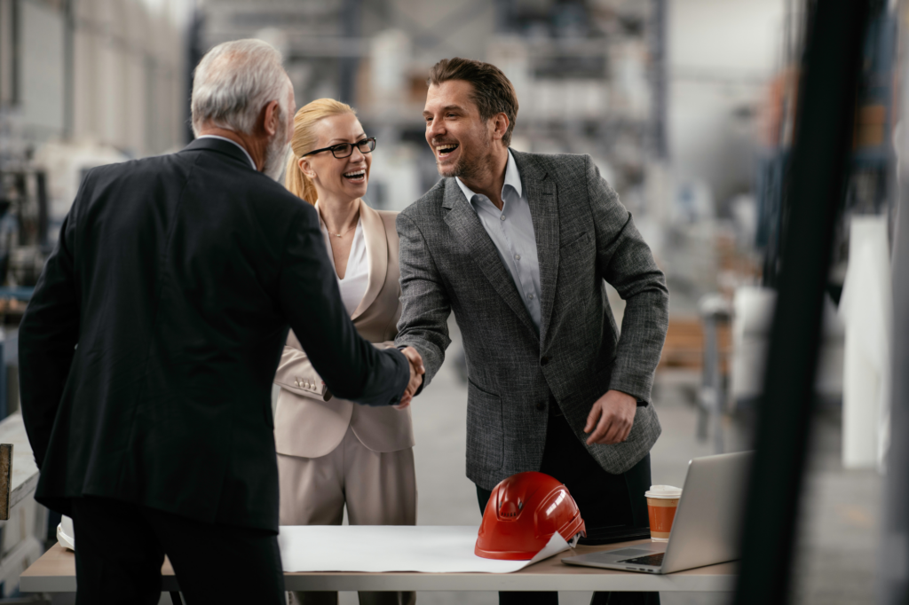 Man enthusiastically shakes another man's hand as a woman smiles at them approvingly, concept photo of chemicals manufacturing business owners getting financing and moving ahead in business