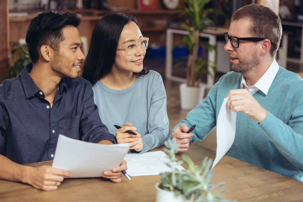 Business owner couple sitting with a loan specialist to discuss business loans, young couple sitting across a man holding up a document.