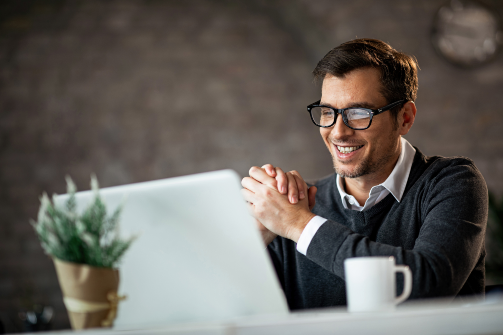 Man in glasses and gray sweater smiles as he reads the display of his laptop, concept photo for making the right choice between business loans, equity financing, and bootstrapping