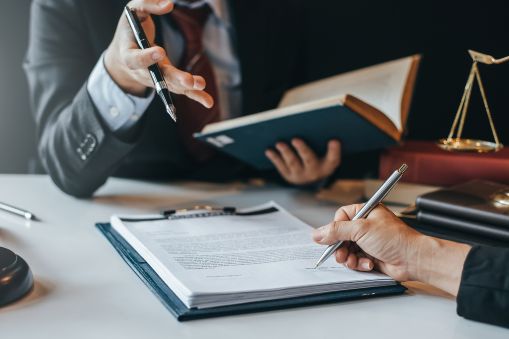 Two professionals discussing and signing legal documents, cropped photo of sharply dressed professionals, documents and law scale visible on the table, concept photo for applying for a caveat loan.