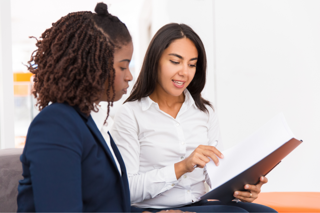 A woman discusses contents of a document with a client, two women in business attire, concept photo for a lender, lending representative, or loan broker explaining a caveat loan