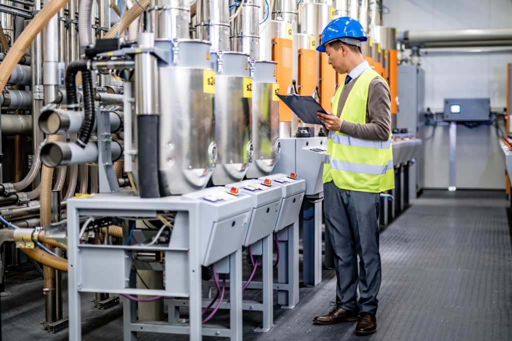 Inspector or worker in hard hat and hi-visibility vest examines plant machinery in food manufacturing plant