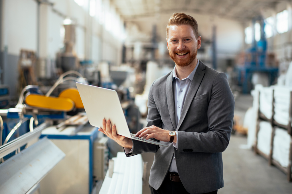 Man in suit smiles while carrying laptop, he is inside a food manufacturing plant or factory, business owner, concept photo for food manufacturing business owner getting immediate funding for business growth