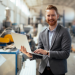 Man in suit smiles while carrying laptop, he is inside a food manufacturing plant or factory, business owner, concept photo for food manufacturing business owner getting immediate funding for business growth