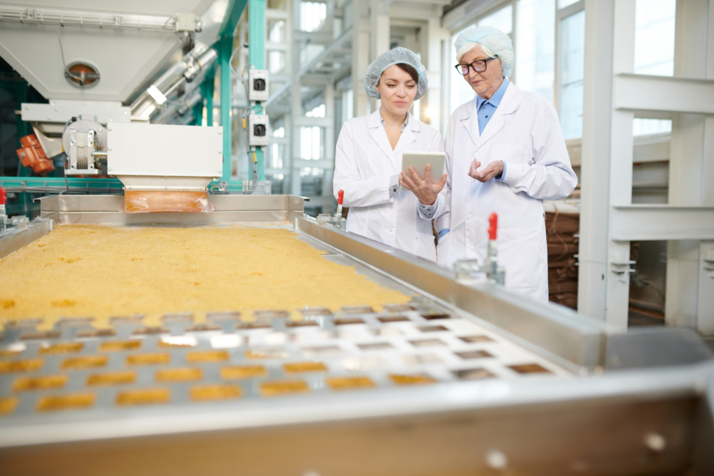 Workers in safe attire, white coat, employees in a food manufacturing plant examining files, machinery visible