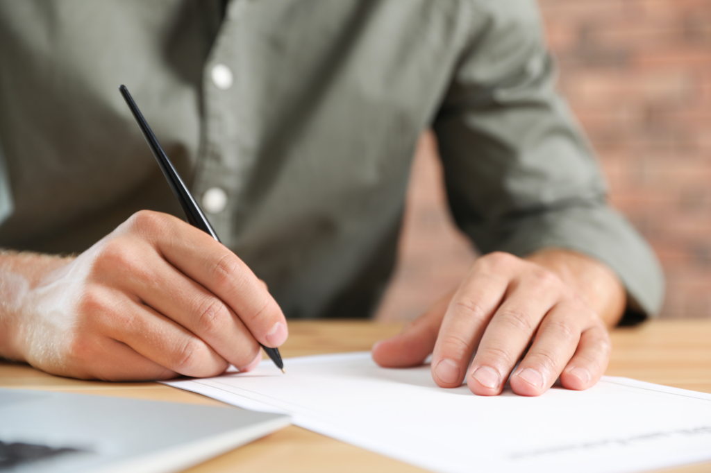 Cropped photo of a man in a grey shirt holding a black pen, signing a document at the bottom. Concept photo for someone applying for a debt consolidation loan in Australia