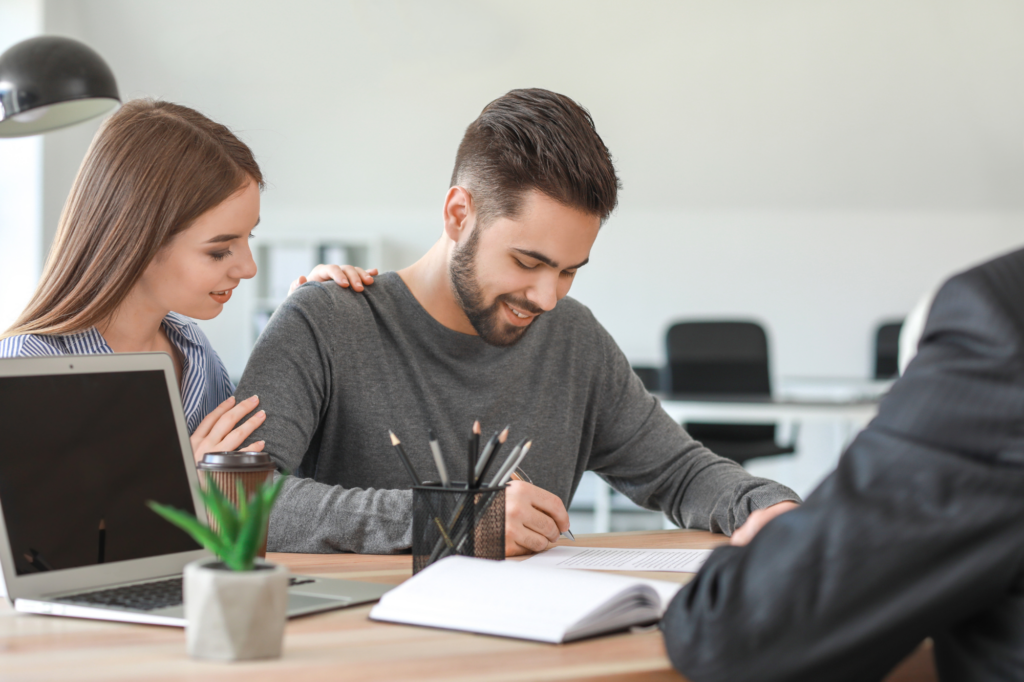 A couple happily signs loan documents in front of a lender or loan expert or broker, signing debt consolidation loan agreement