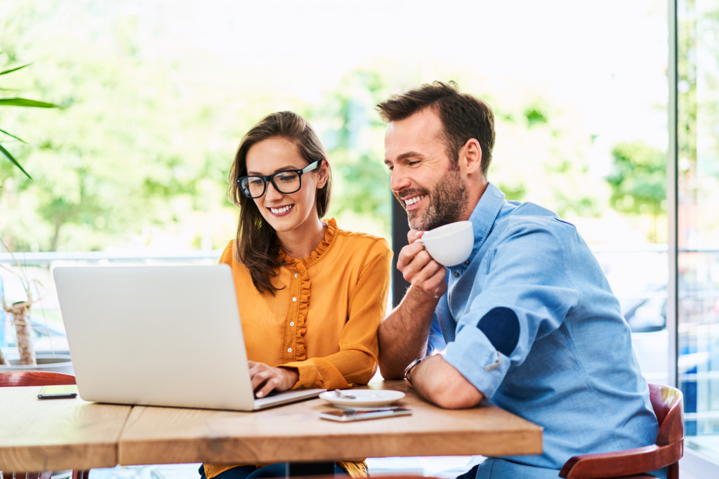 A man and a woman smiling while reading the screen of a laptop, bright cafe, concept photo for business partners getting a private loan approved