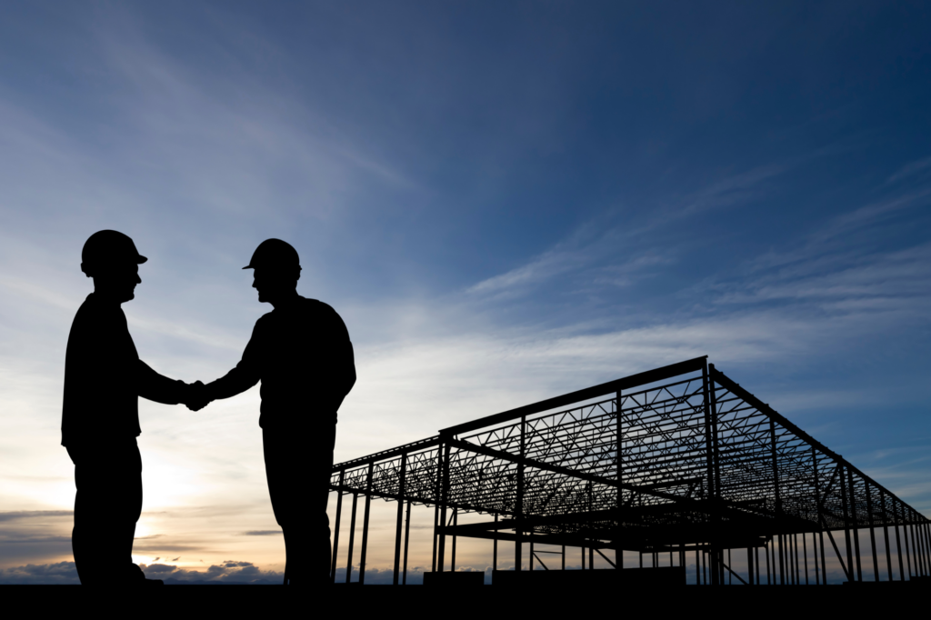 Atmospheric silhouette photo at dusk, two construction professionals shake hands in front of a steel foundation for a building