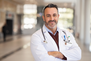 Doctor with crossed arms smiles directly into camera, smiling doctor, photo with out of focus background, concept photo for doctor who got approved for a medical business loan