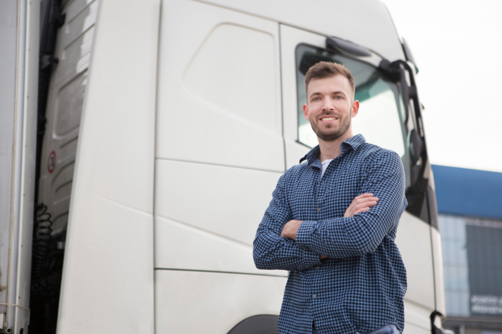 Man with crossed arms smiling while posed at the side of a large truck