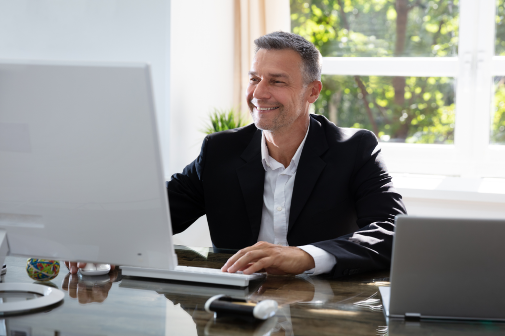 A man in a suit smiles as he uses his desktop computer, a businessman paying off tax debt with the ATO