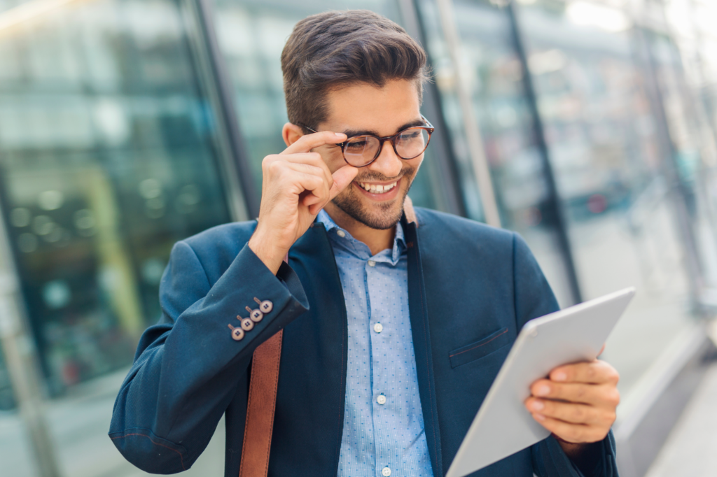 A man in a suit adjusts his glasses as he happily reads the screen of an electronic tablet, businessman successfully dealing with tax debt