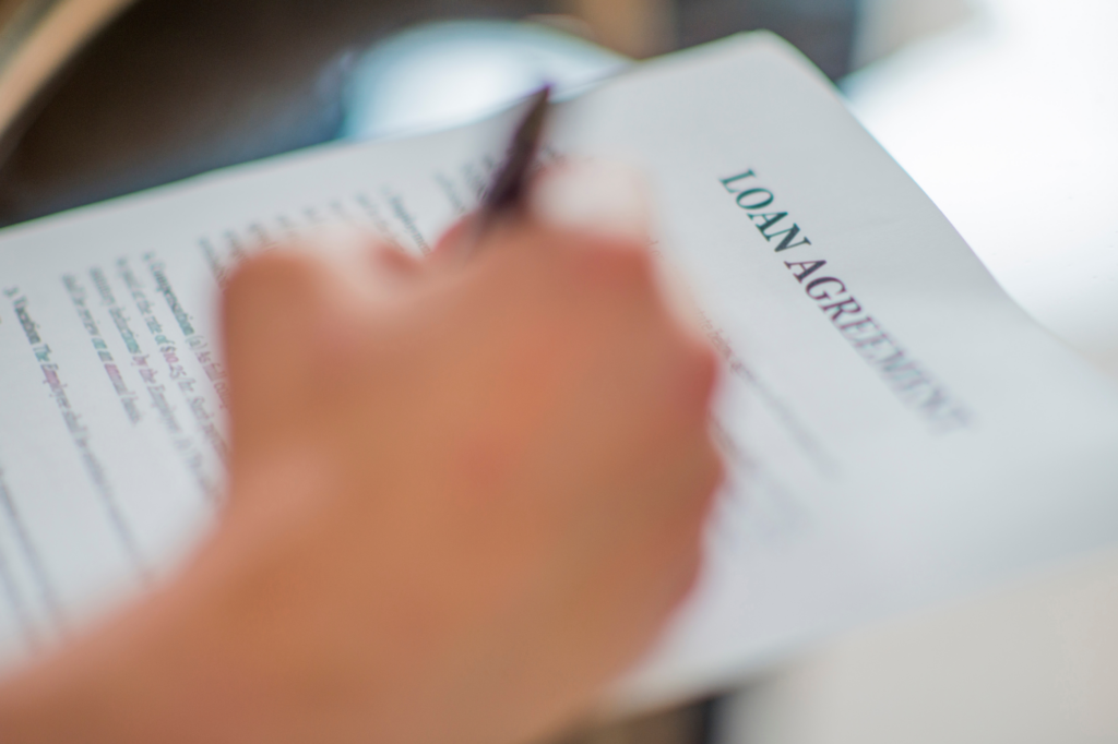 Unfocused photo of a hand signing a loan agreement, signing an unsecured business loan agreement