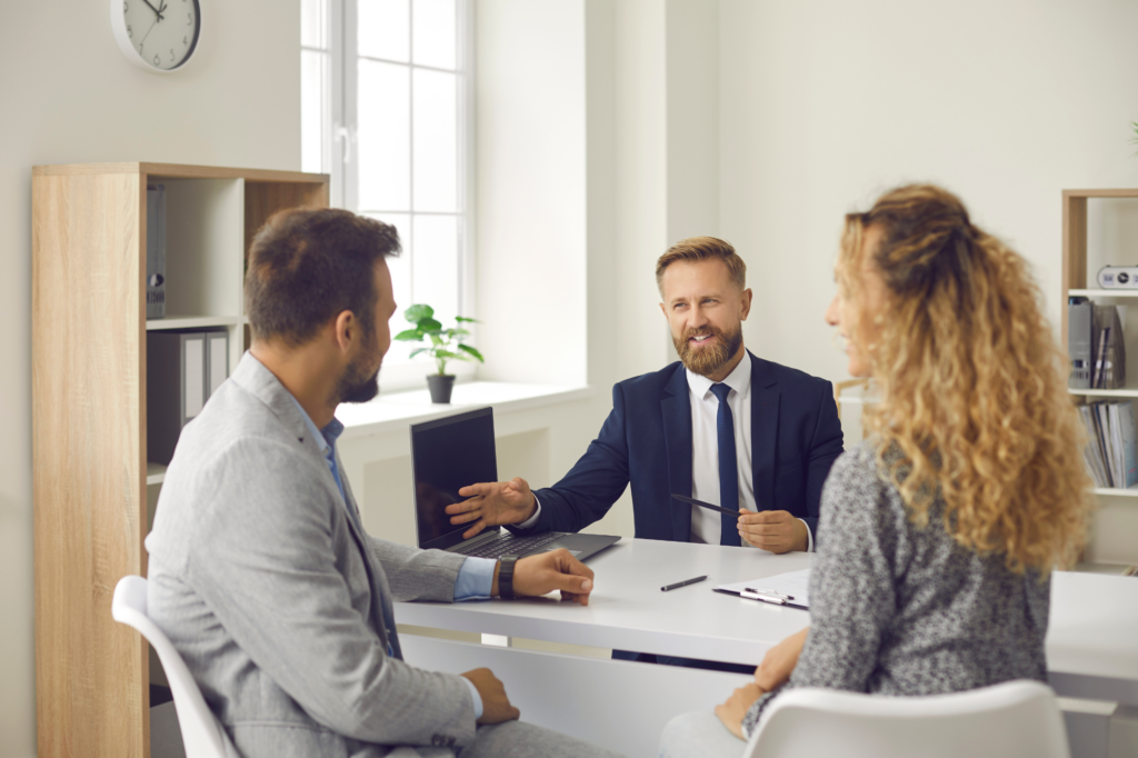 A man and woman sit across the table from a man, having a spirited discussion, laptop and clipboard visible on the table, concept photo for discussing advantages and disadvantages of cash flow lending