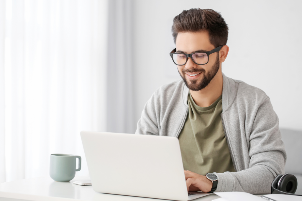 Brightly lit photo of a man in a grey jacket typing cheerfully on his laptop, concept photo for business owner accessing funding through an unsecured business overdraft