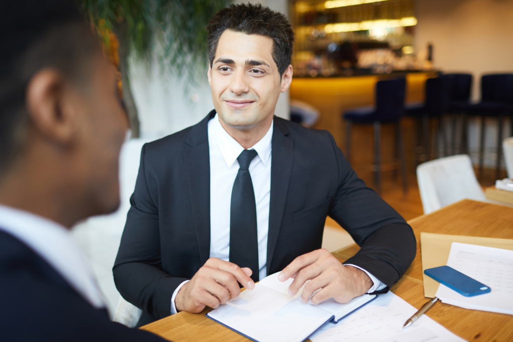 Man in a suit smiles as he is talking to another man seated across him, photo of a business owner listening to a private lending offer