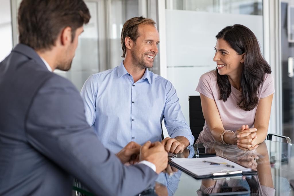 A couple happily look at each other while seated across a man in a suit, concept photo for business owners agreeing on a loan from a private lender