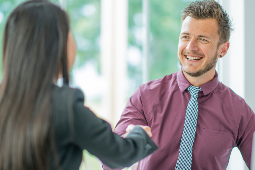 A man happily shakes a woman’s hand, professional setting, concept photo for business owner and private lender agreeing to loan terms