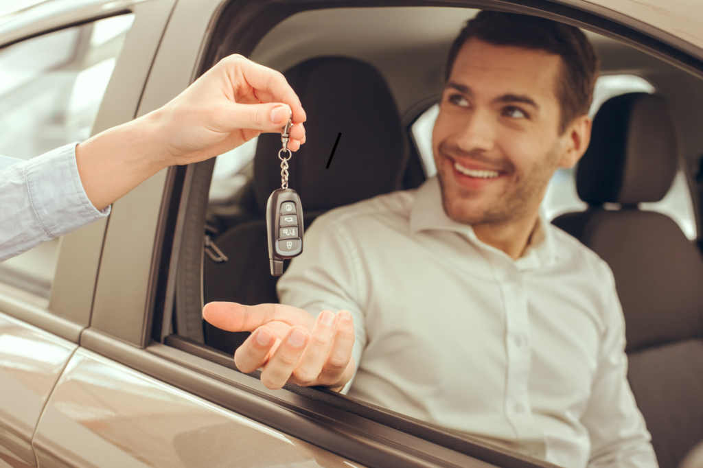 A man seated in a car’s driver seat happily accepts the keys to his new car after getting his car loan approved