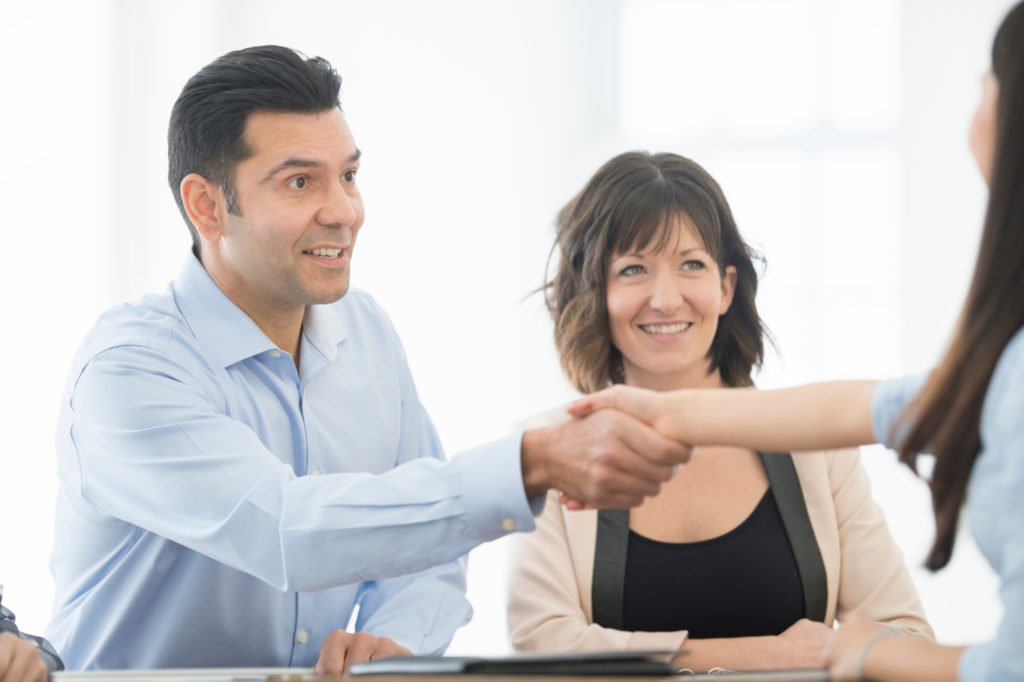 A man seated next to a woman shakes the hand of another woman seated across them from the table, concept photo of business owners getting low doc loan approval