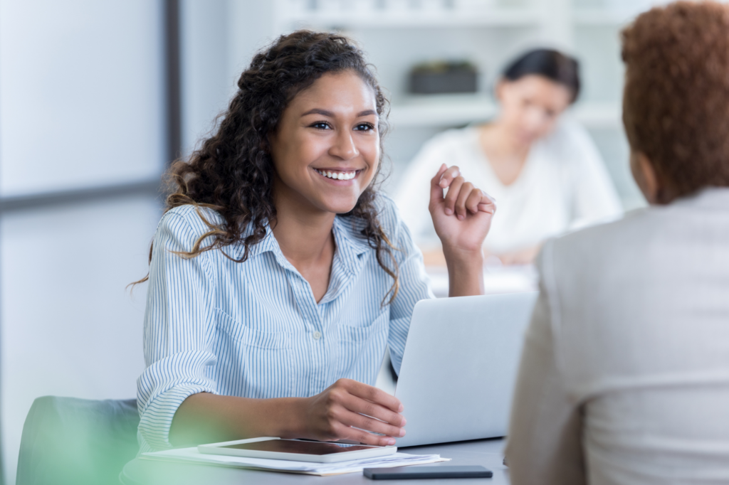 A woman cheerfully talks with a man seated across her from a table, a business owner agreeing to tax debt loan terms with a lender or broker