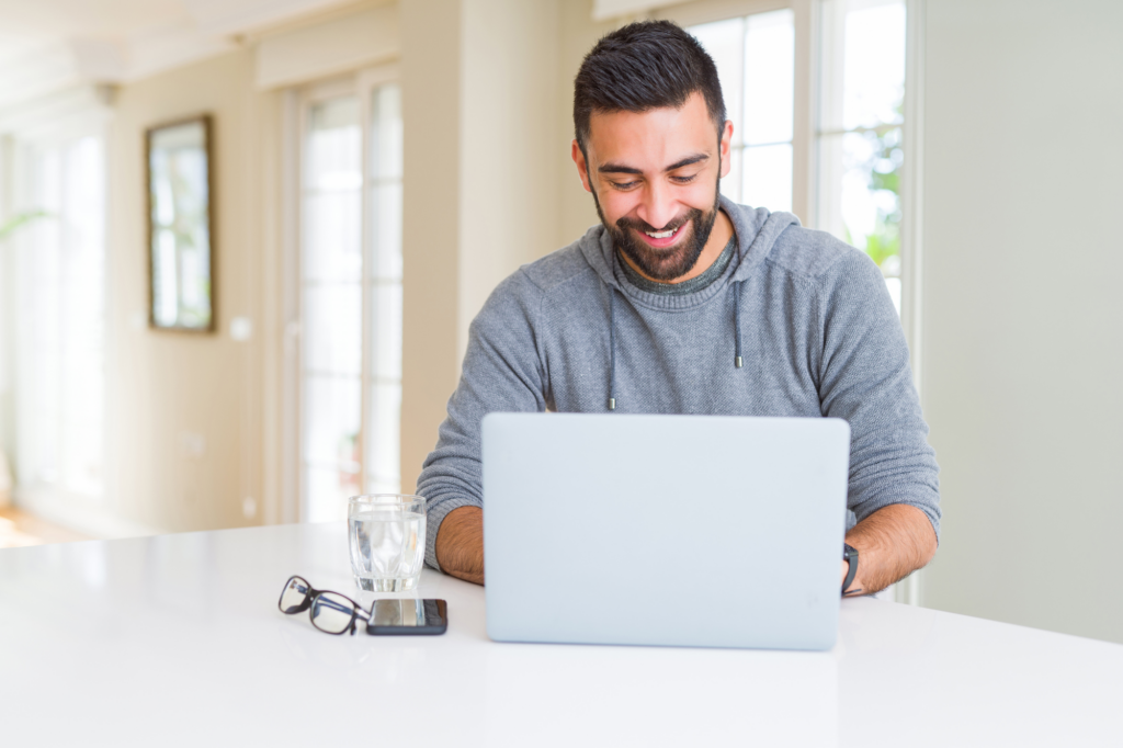 A man smiles as he types on his laptop, concept photo of a business owner applying for a no doc or low doc business loan online