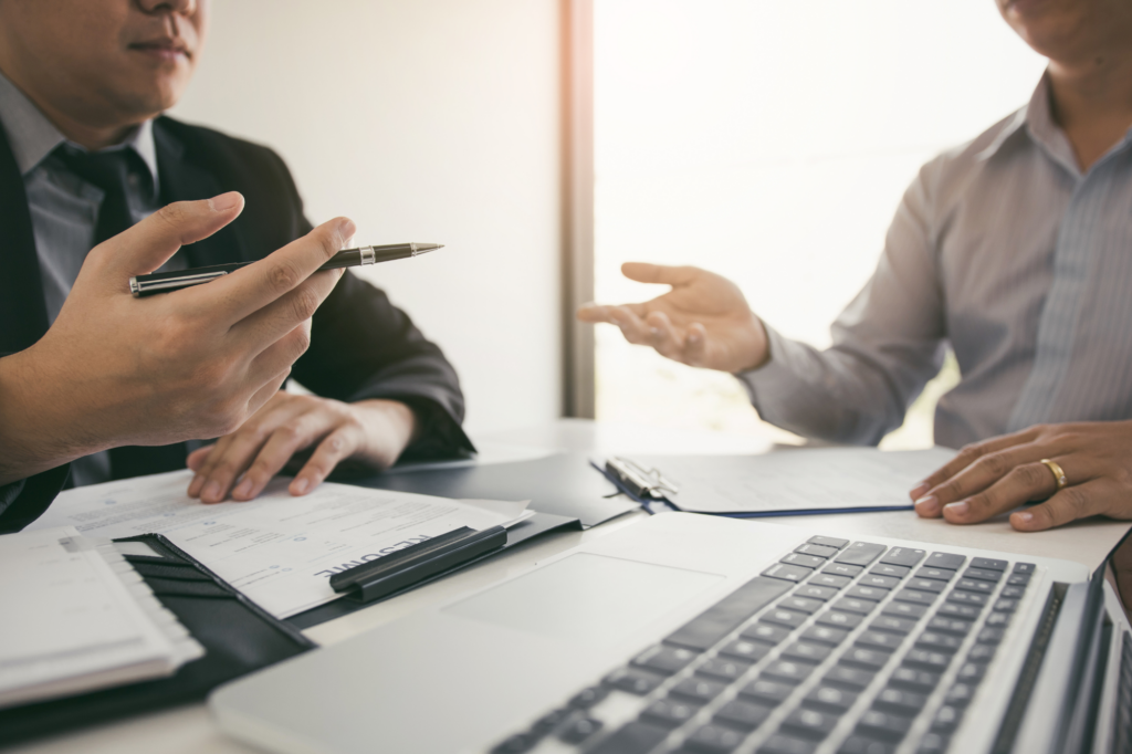 Cropped photo of two men in animated discussion with documents and laptop visible on the table, client and lender or broker meeting about SMSF loans requirements