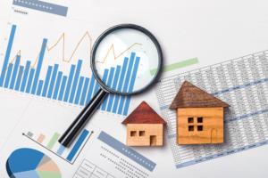 Various documents with graphs and charts layered on top of each other, with a magnifying glass and two wooden model houses on top, concept photo for debt recycling in Australia