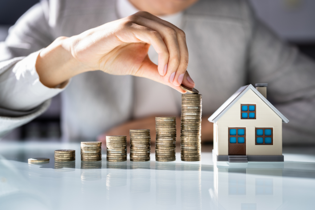 Cropped photo of a man stacking coins in piles of ascending order with a white miniature model house next to the last pile, concept photo of building equity in your home