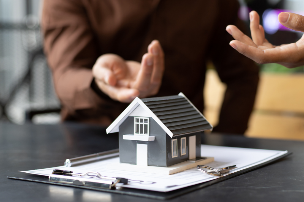 Cropped photo of two people in a discussion with a model miniature house in the foreground, discussion about using personal assets for SMSF Loans