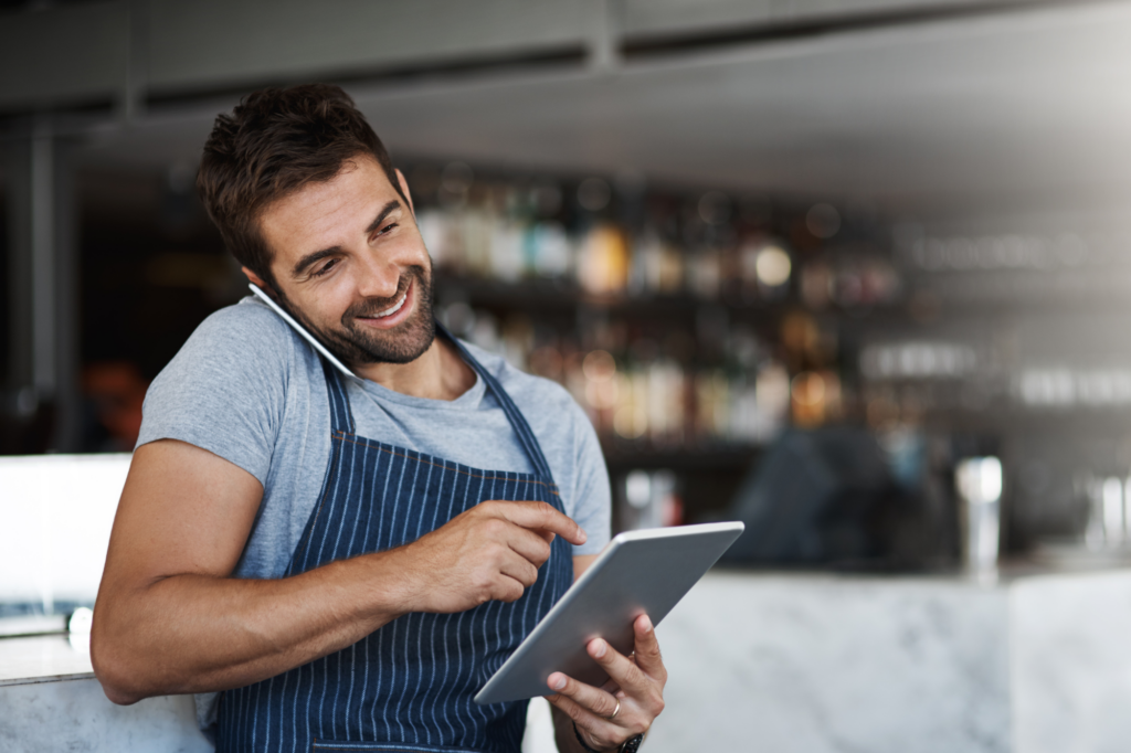 A man cheerfully talks on his cellphone while holding an electronic tablet, concept photo of a business owner arranging the purchase of goods using an import finance facility