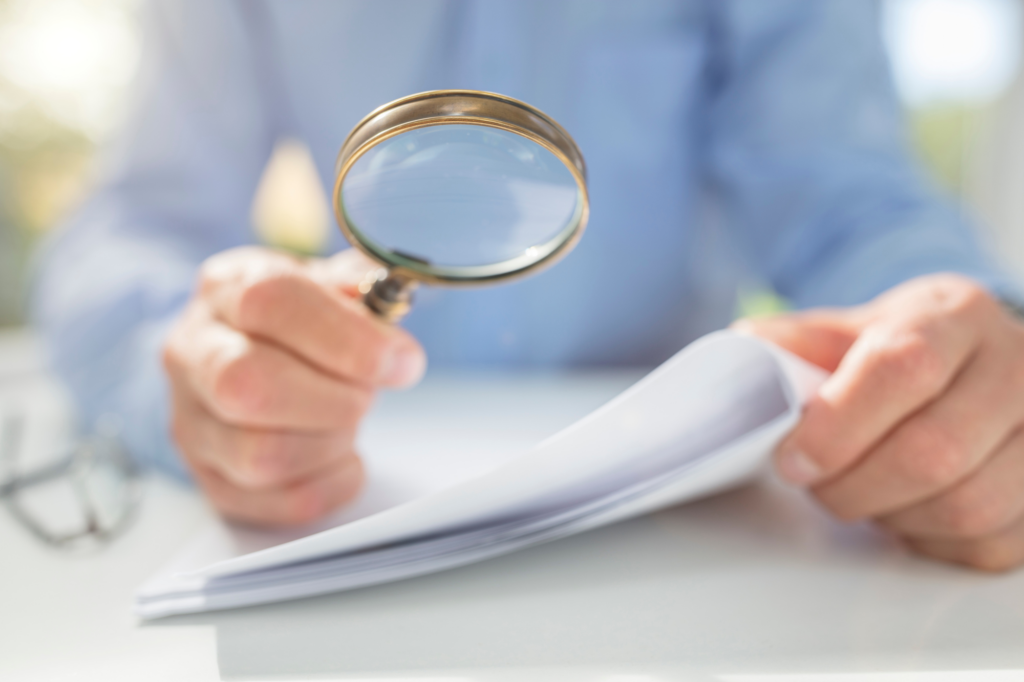 Zoomed cropped photo of a man using a magnifying glass to read a document better, concept photo for reading the fine print on tax debt loans