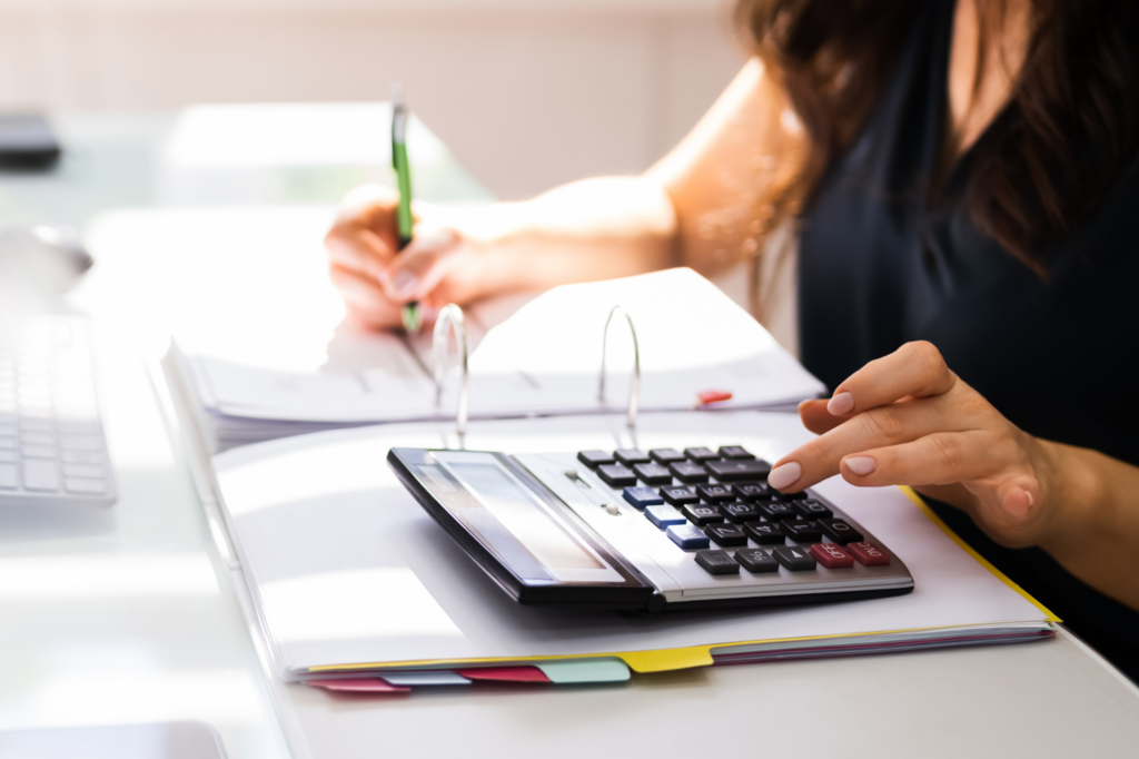 A woman reviewing her taxes, writing on paper and using a calculator, concept photo for a woman considering an ATO payment plan for her tax debt