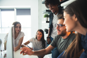 A group of business owners happily discuss funding for their business, looking at a computer monitor, discussing startup business loans