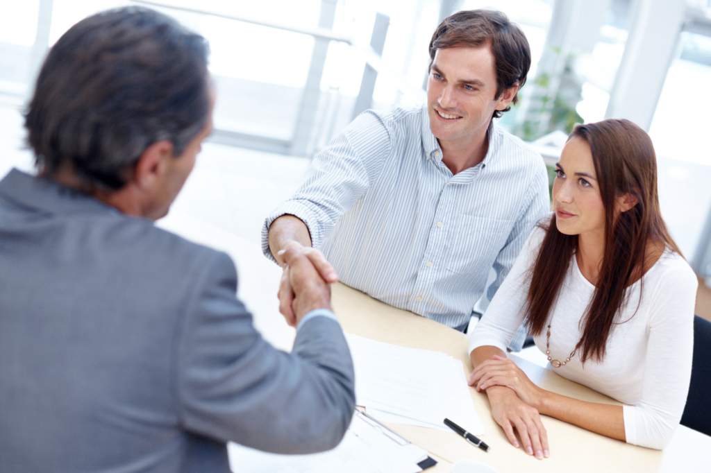 A couple sits across and shakes hands with a man in a suit, concept photo for borrowers getting a private loan approved.