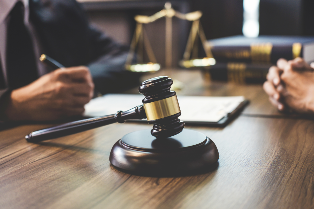 A close-up photo of a gavel with two people and a law scale in the background, a concept photo to represent the legality of debt recycling