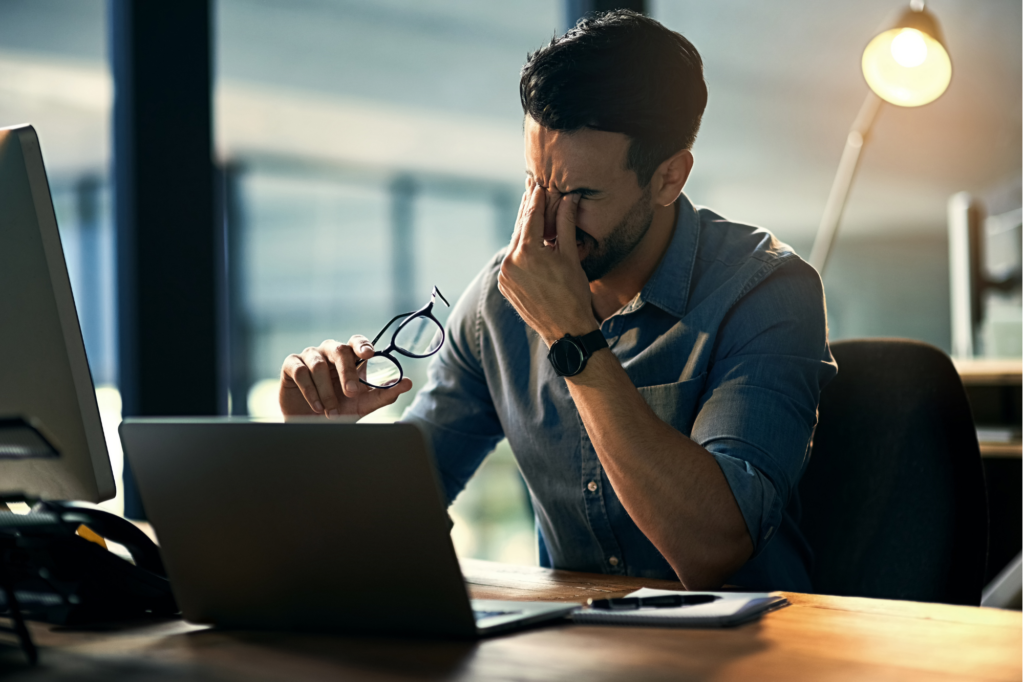 A man takes a break from reading the screen of his laptop by taking off his glasses and massaging his eyes, concept photo for stress because of complicated investment strategies