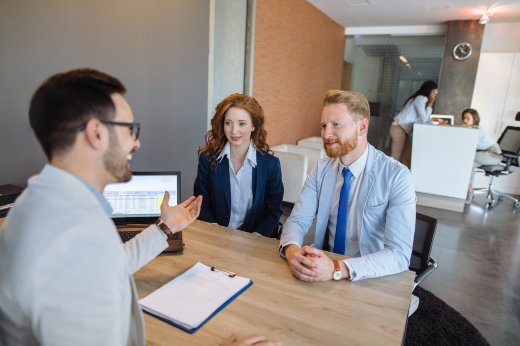 A man and a woman sit across a man with a laptop and documents, discussion or client meeting for a tax debt loan, broker or lender explaining the benefits of tax debt loans for tax debt relief