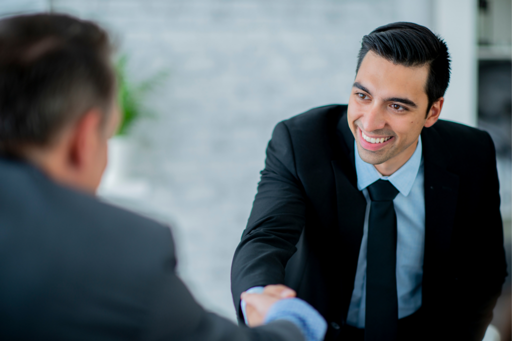 A man in a suit leans forward and shakes the hand of another man, smiling, happy, businessman who got a tax debt loan approved by a lender