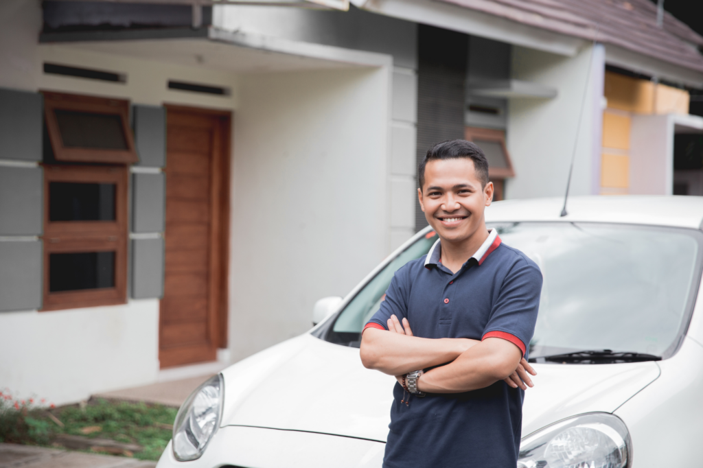 A man happily poses with his arms crossed in front of his brand new car after his car loan got approved.