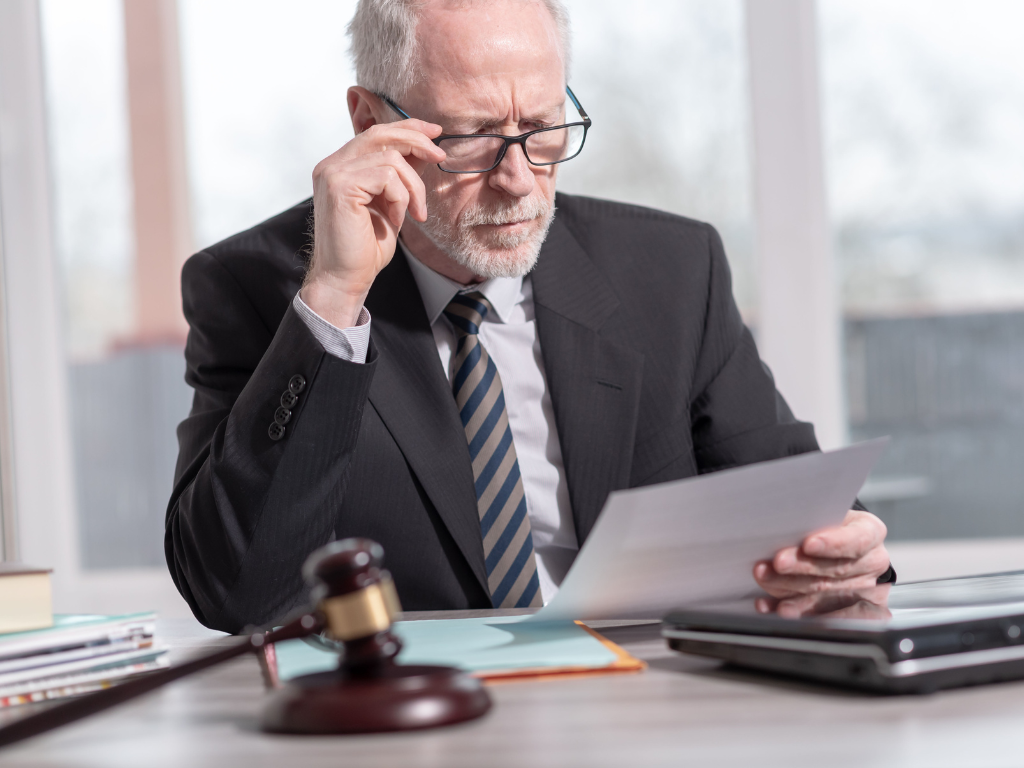 An older man in a suit and wearing glasses carefully reads a legal document, concept photo of someone receiving a notice to complete