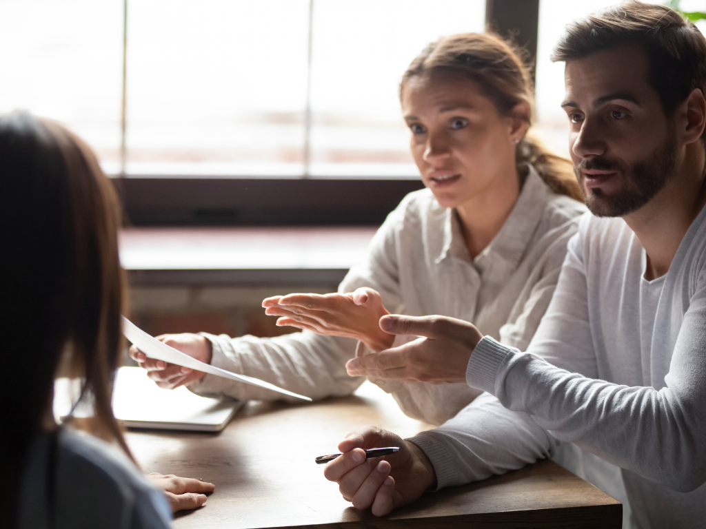 A man and a woman engage in tense discussion with another woman regarding a contract, concept photo of buyers challenging a notice to complete